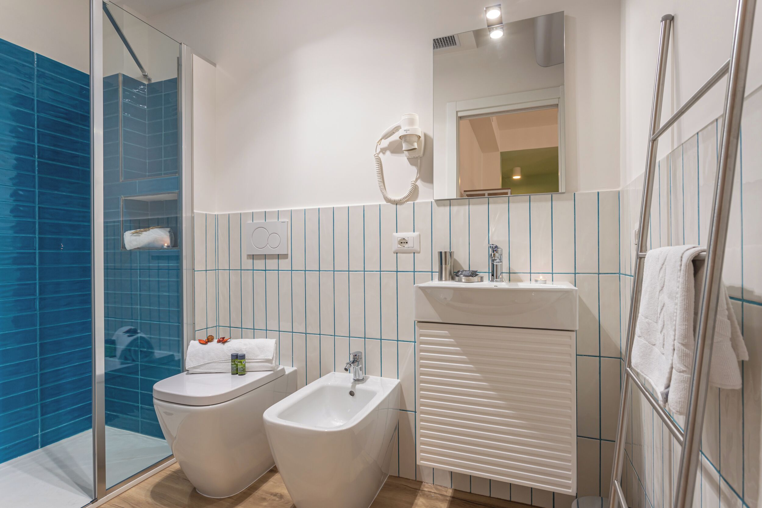 A modern bathroom with a glass shower enclosure, a bidet, a toilet, and a sink with a mirror above.