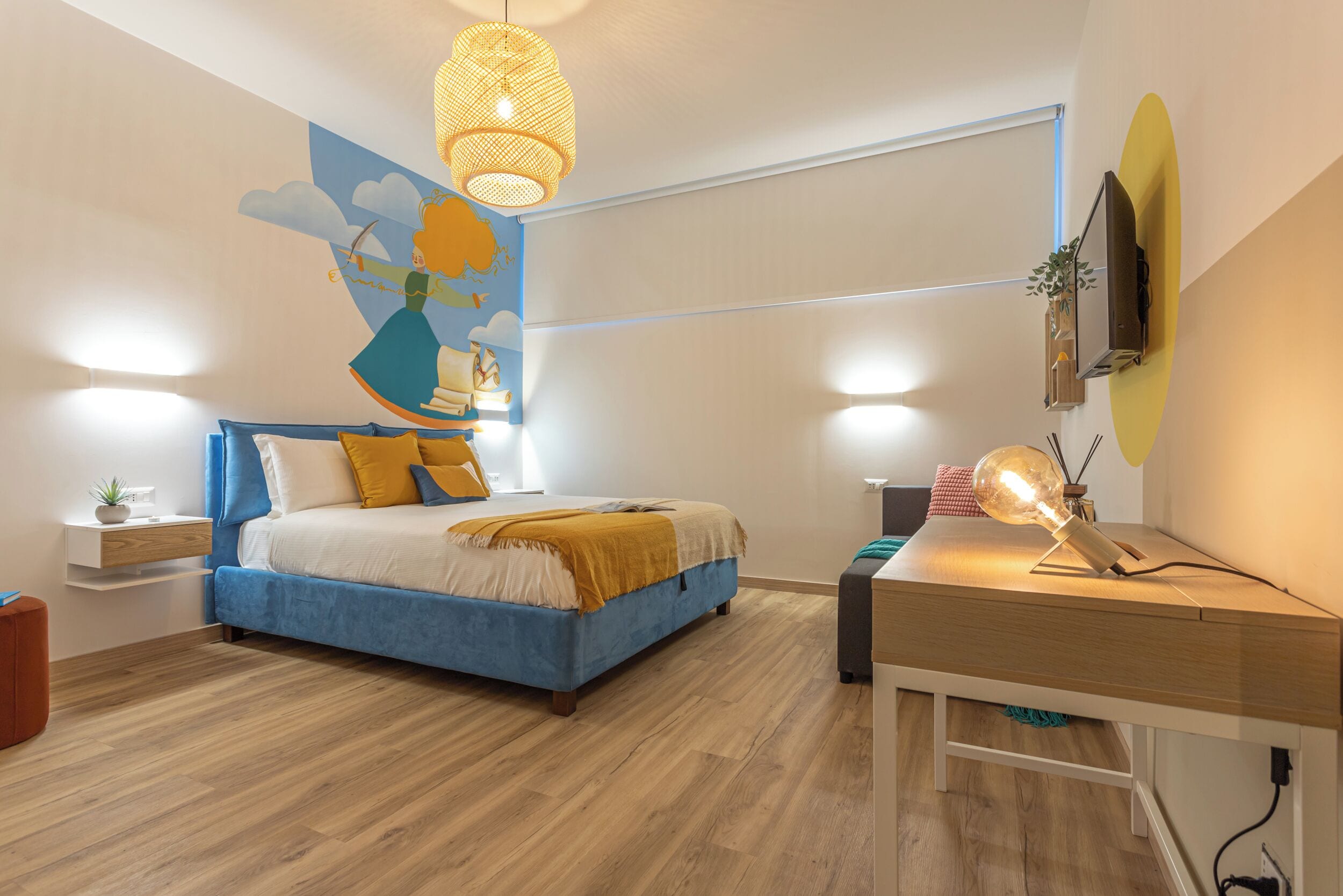 A modern bedroom with a bed, bedside table, lamp, and a wall mural.