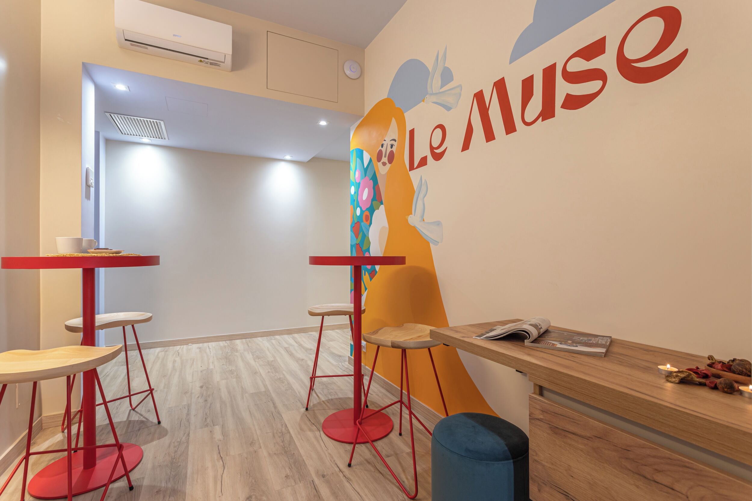 Een modern interieur met een receptiebalie, twee rode barstoelen en een muur waarop 'Le Muse' staat.