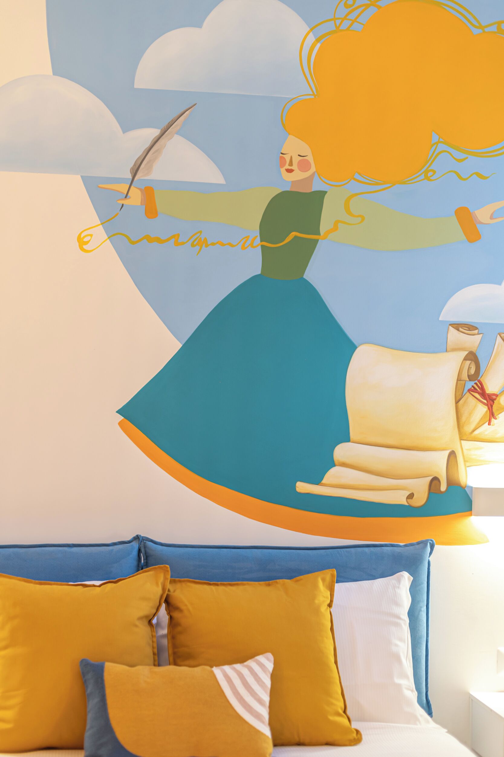 A room with a mural of a woman flying, a blue sofa, and yellow pillows.