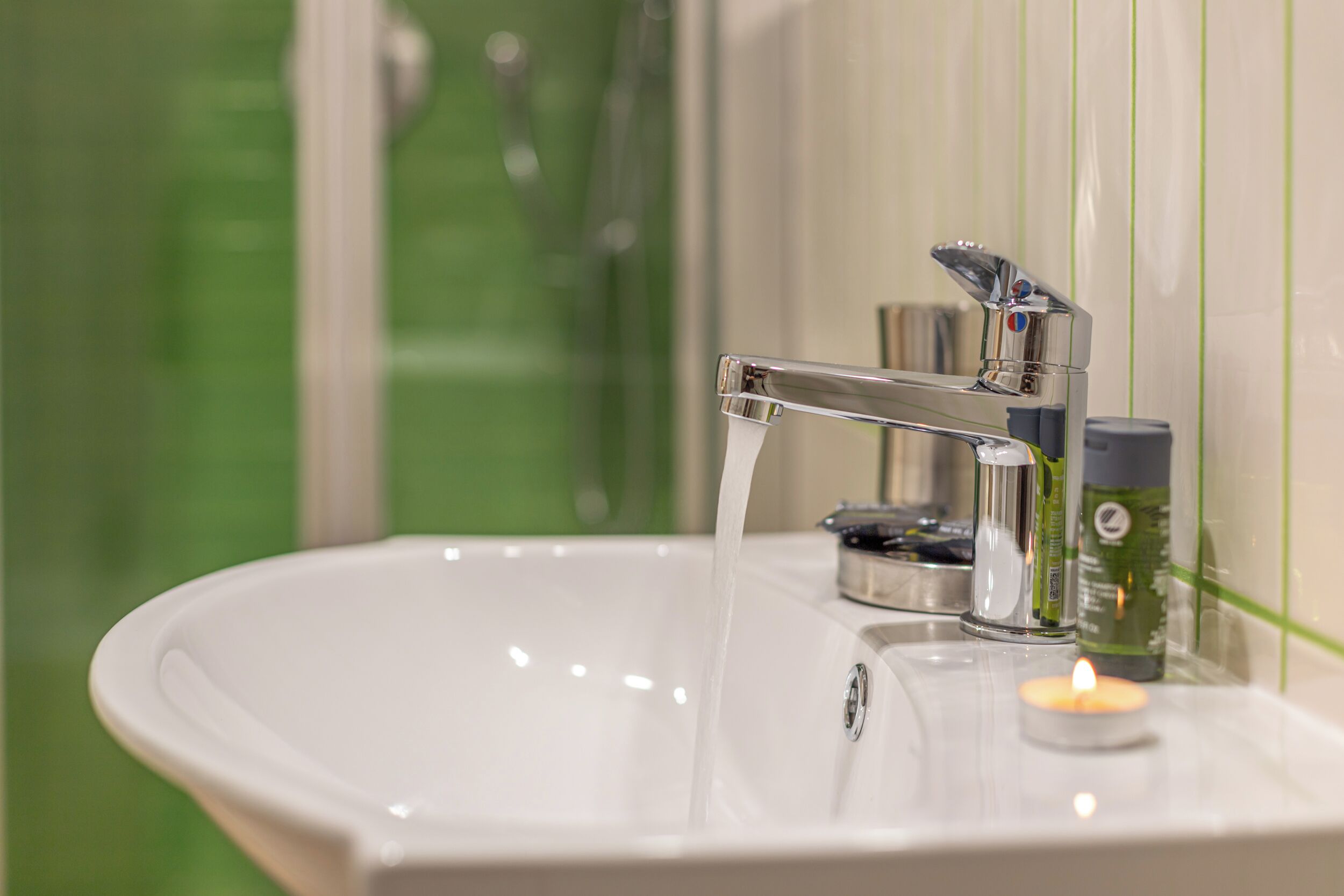 A bathroom sink with running water, a mirror, and a candle.