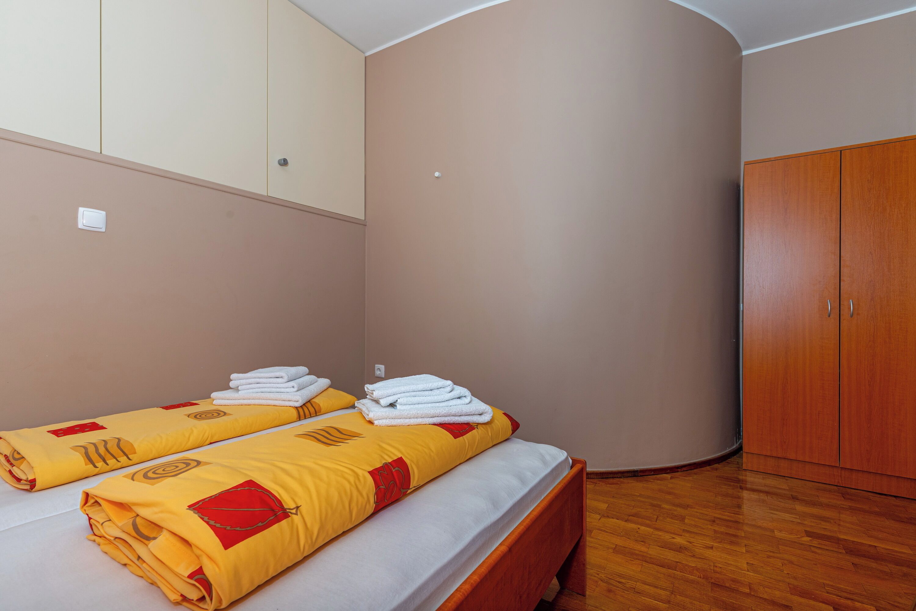 A room with two beds, wooden wardrobe, and a curved wall.