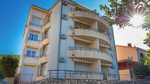 A multi-story building with balconies, air conditioning units, and a stone wall in front. - Apartman Mira (Crikvenica)