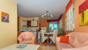 A modern living room with a sofa, a dining table, and chairs. There is a kitchen in the background with cabinets and a refrigerator. - Apartman Mira (Crikvenica)