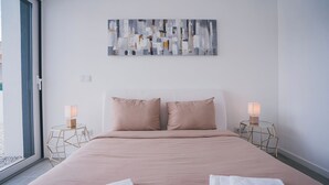 Ein Schlafzimmer mit einem großen Bett, zwei Nachttischen mit Lampen, einem Wandbild und einem Fenster mit Aussicht.