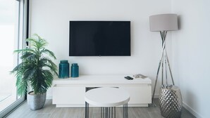 Ein modernes Wohnzimmer mit einem wandmontierten Flachbildfernseher, einem weißen Konsolentisch, einer Topfpflanze und einer Stehlampe.