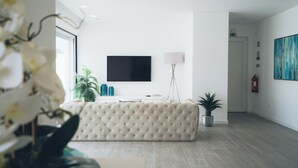 Eine moderne Hotelhalle mit einer gesteppten Couch, einem Flachbildfernseher, einer Stehlampe und einem Topf mit Pflanze.