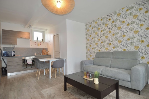 Una cocina moderna con un cartel que dice 'Cook', un comedor con sillas, un sofá gris y una mesa de centro con objetos decorativos.