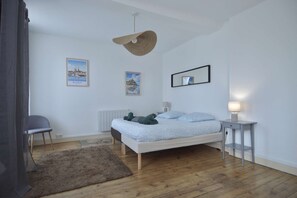 Un dormitorio con cama, una mesita de noche con lámpara, un radiador, una silla y dos cuadros en la pared.