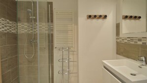 Un baño moderno con ducha de vidrio, un lavamanos blanco y un espejo.
