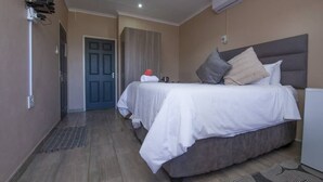 A hotel room with a bed, a door, an air conditioning unit, and a radiator. - The Rock at Edwaleni (Matsapha)