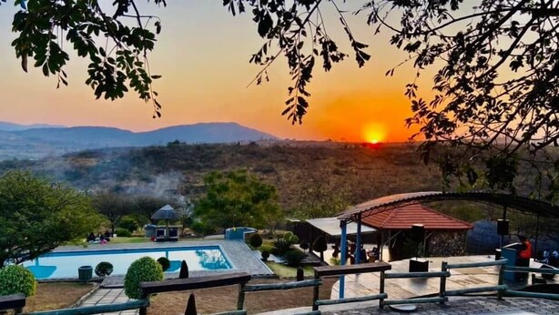 A pool area with hexagonal tiles, a gazebo, and a view of the sunset over a hilly landscape. - The Rock at Edwaleni (Matsapha)