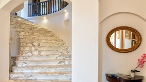 A marble staircase leading to a second floor, a round mirror on the wall, and a small table with a potted plant and books. - Sardinia RE - Dimora Della Contessa (Alghero)