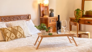 A neatly made bed with a decorative headboard, a bedside table with a bottle and glass, and a small potted plant. - Sardinia RE - Dimora Della Contessa (Alghero)