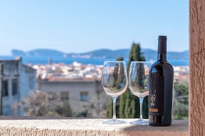 A wine bottle and two glasses on a balcony overlooking a coastal cityscape. - Sardinia RE - Dimora Della Contessa (Alghero)