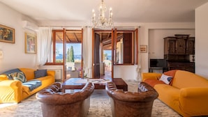 A living room with a yellow sofa, a brown leather ottoman, a wooden coffee table, and a chandelier. - Sardinia RE - Dimora Della Contessa (Alghero)