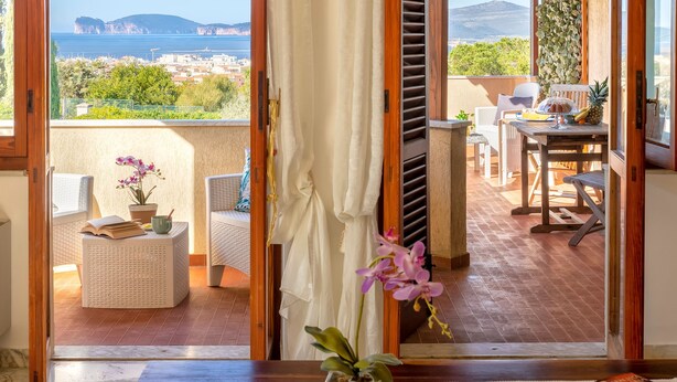 A balcony with a view of the sea, a table with chairs, and a potted orchid. - Sardinia RE - Dimora Della Contessa (Alghero)