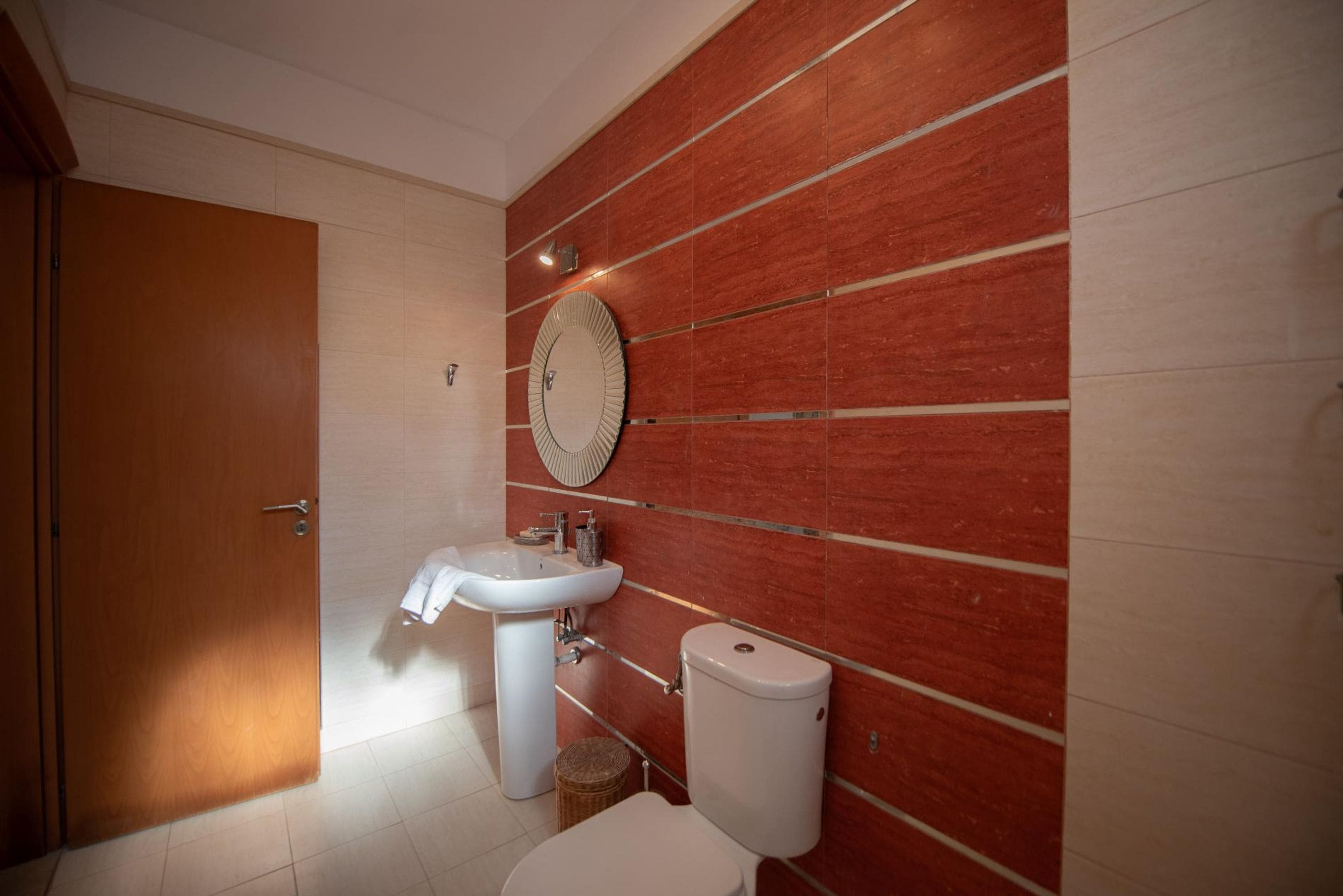 A bathroom with a wooden door, a white sink, a toilet, and a decorative mirror on the wall.