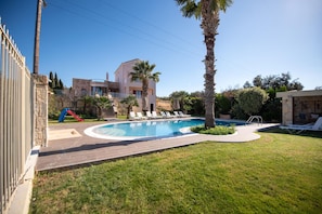 A swimming pool with lounge chairs, a palm tree, and a stone building in the background. - Villa Angels in Crete (Malevizi)