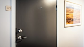 Una puerta negra con cerradura y manija, una placa con el número '201', y un cuadro en la pared.