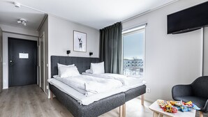 Una habitación de hotel moderna con una cama grande, una mesita con aperitivos, un televisor y una ventana con vistas a la ciudad.