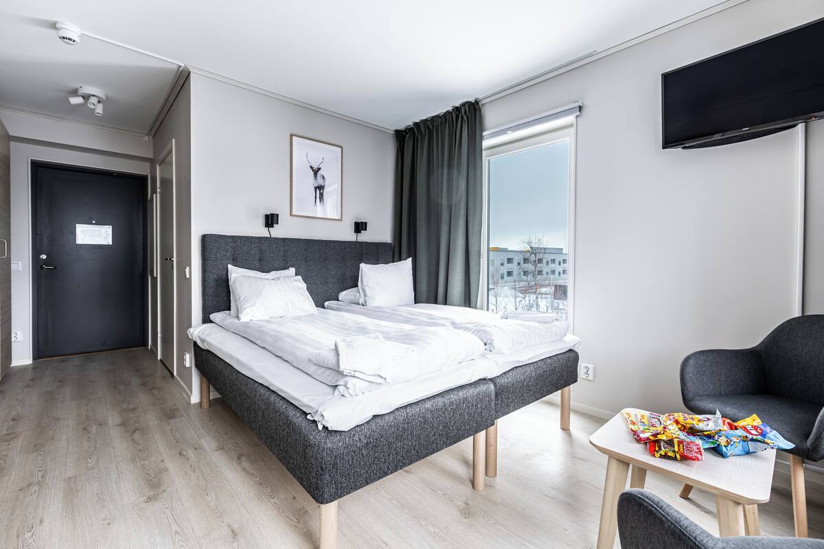 Ein modernes Hotelzimmer mit einem großen Bett, einem kleinen Tisch mit Snacks, einem Fernseher und einem Fenster mit Blick auf die Stadt.