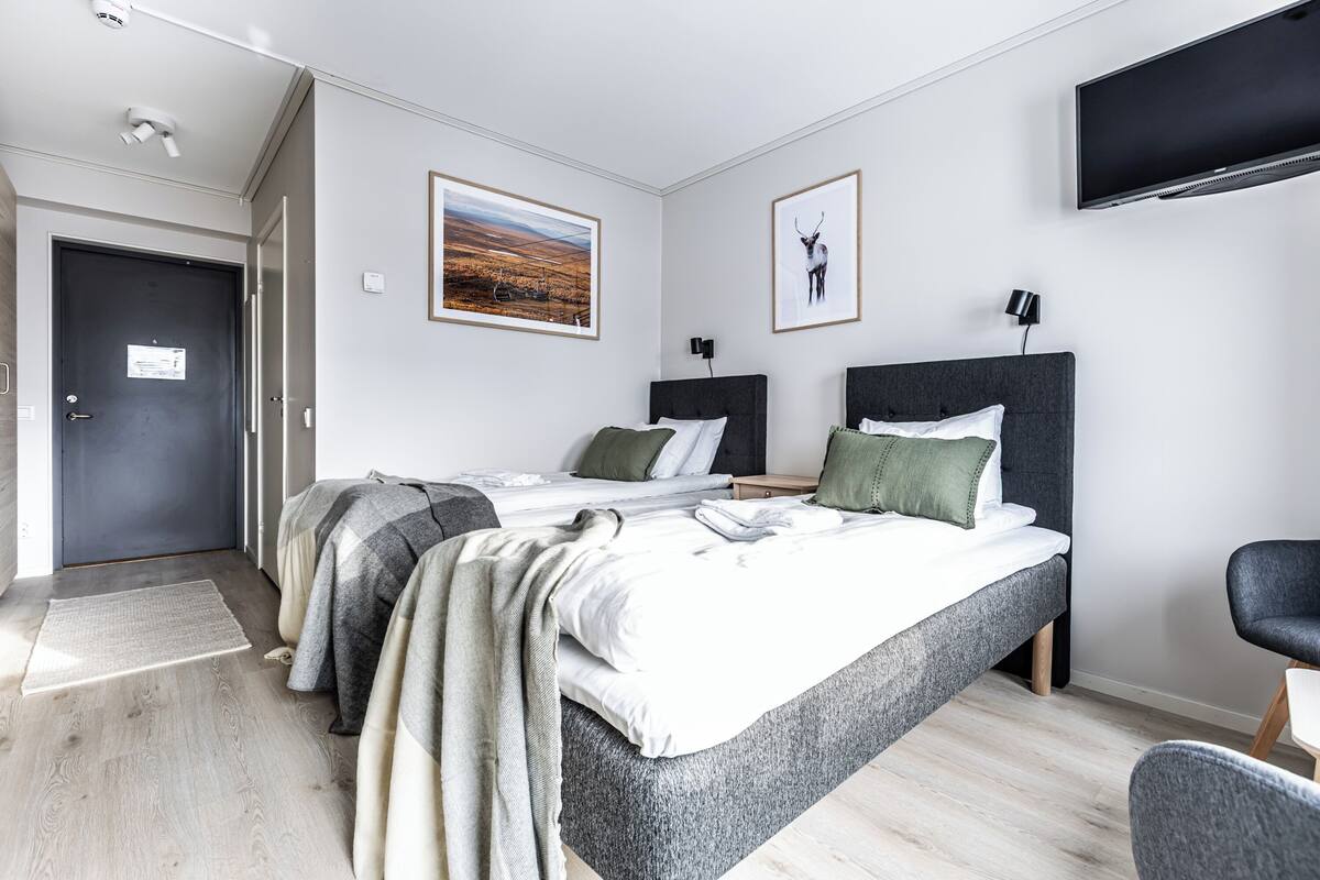 Ein modernes Hotelzimmer mit zwei Betten, einem Flachbildfernseher und Kunstwerken an den Wänden.