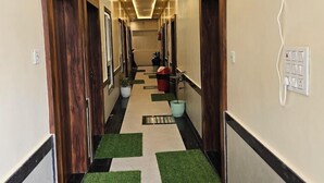 Un pasillo de hotel con puertas de madera, iluminación empotrada, un cubo de basura y un dispensador de agua azul.