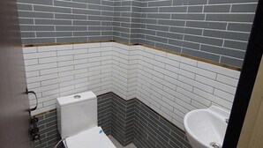 Un baño pequeño y moderno con azulejos blancos y grises, inodoro blanco, lavabo y zona de ducha.