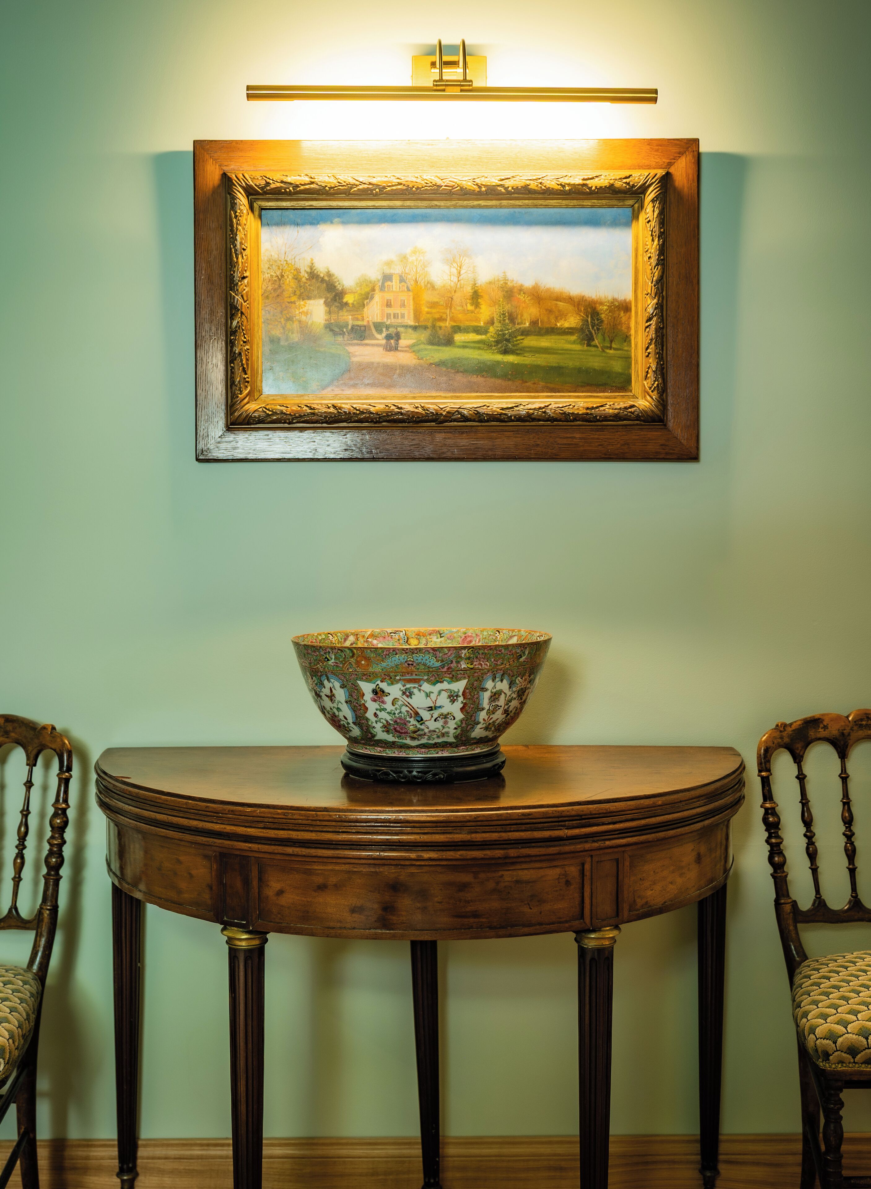 Una mesa de comedor con un cuenco decorativo en el centro, flanqueada por dos sillas. Sobre la mesa, un cuadro enmarcado cuelga de la pared.