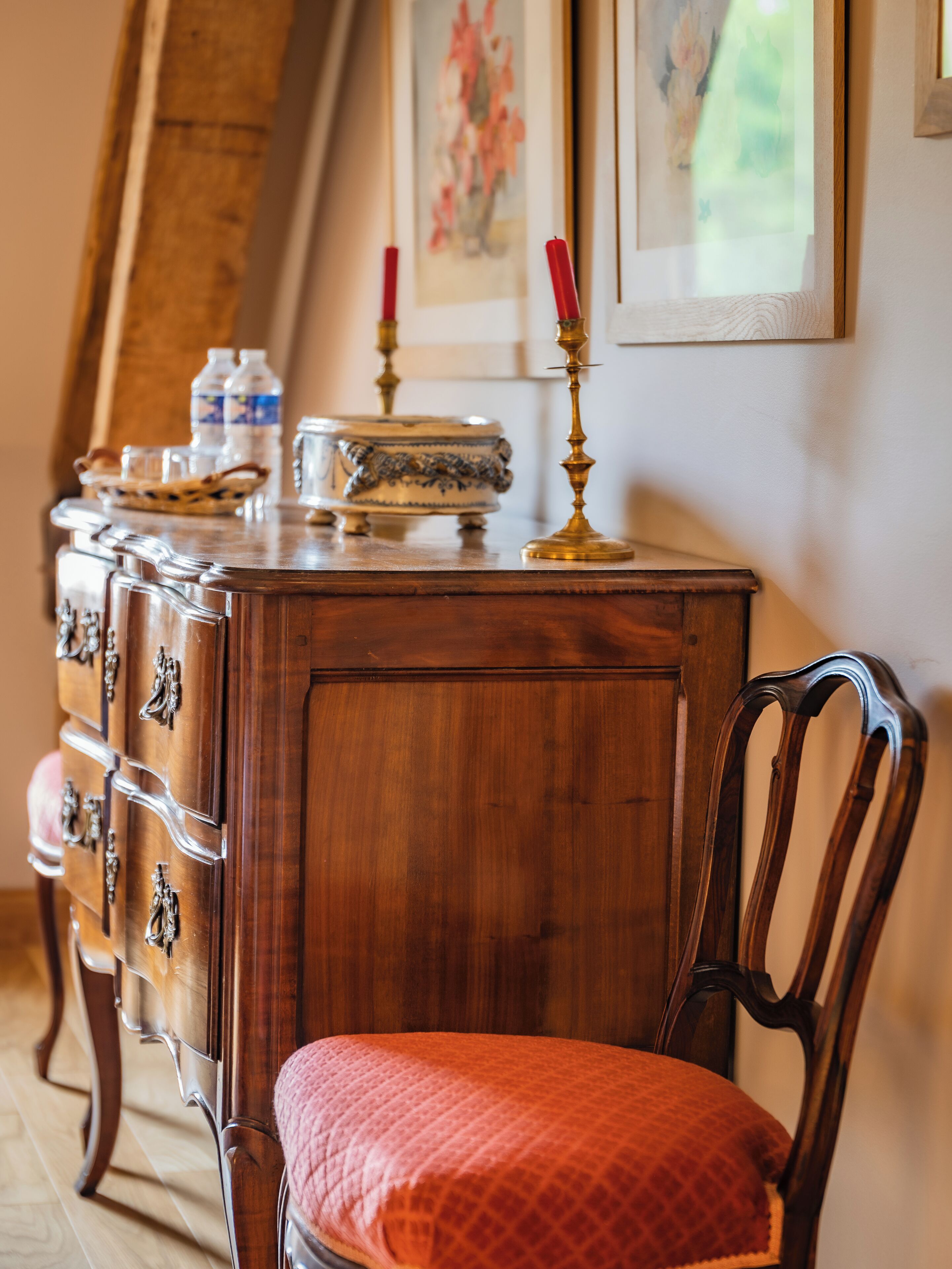 A wooden dresser with drawers and a chair with a red cushion.
