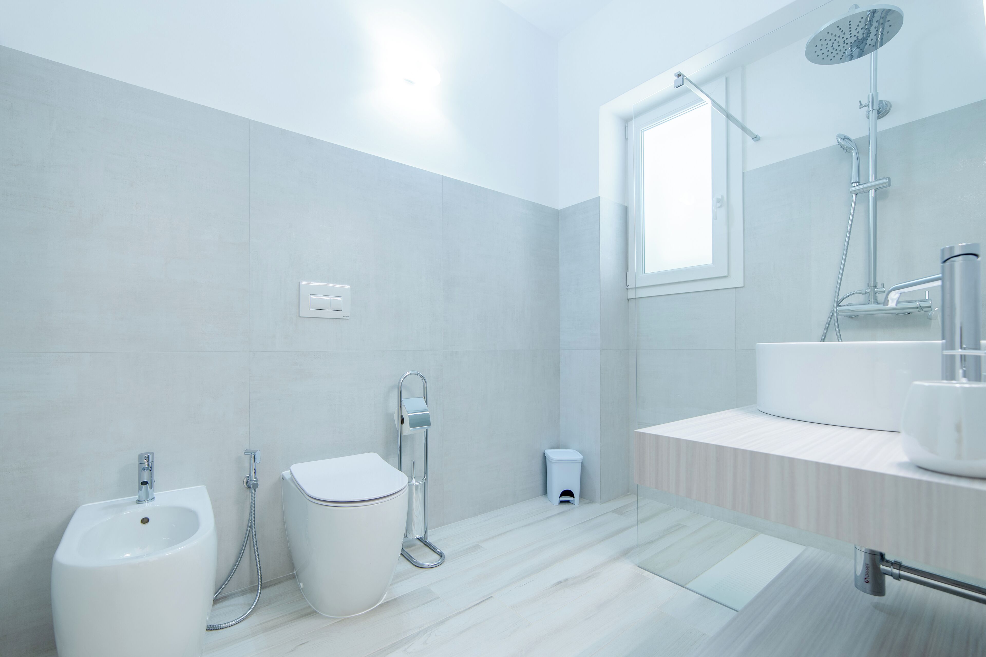 Un baño moderno con bidé, inodoro y un espejo grande sobre un lavamanos.
