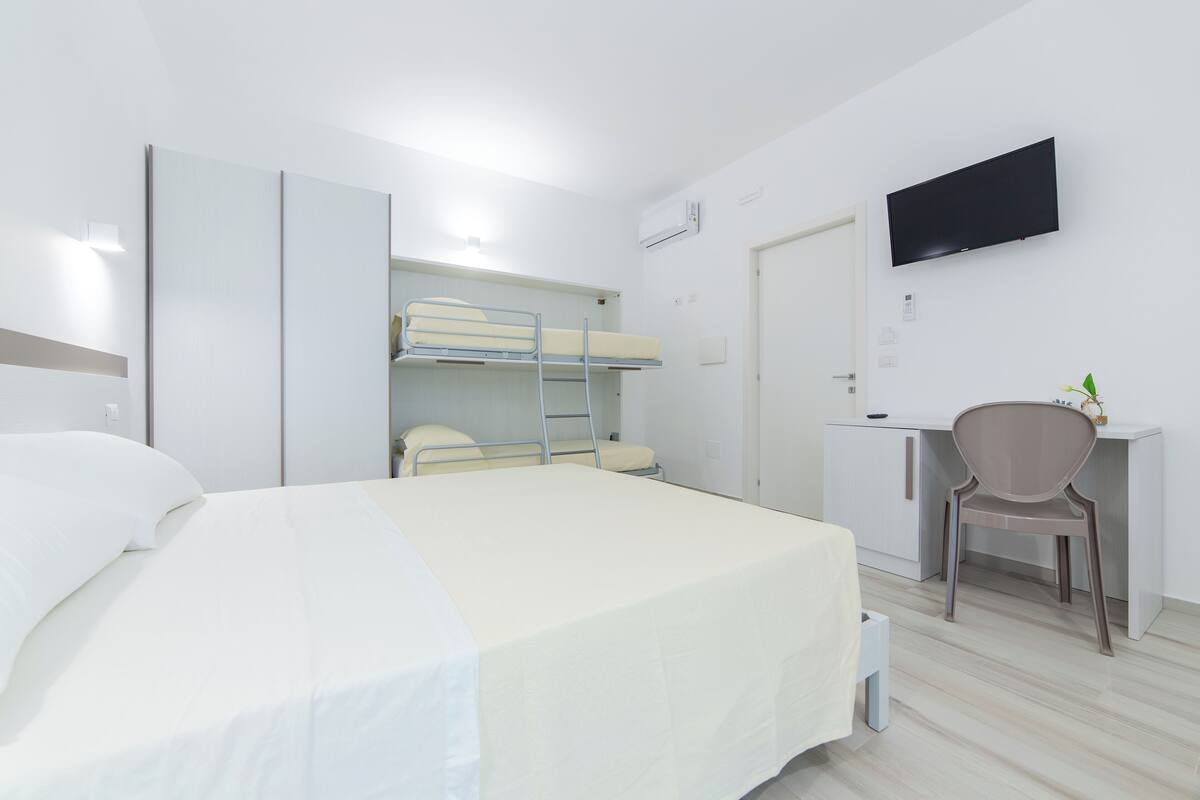 Una habitación de hotel con literas, un escritorio con silla, un televisor y un armario.