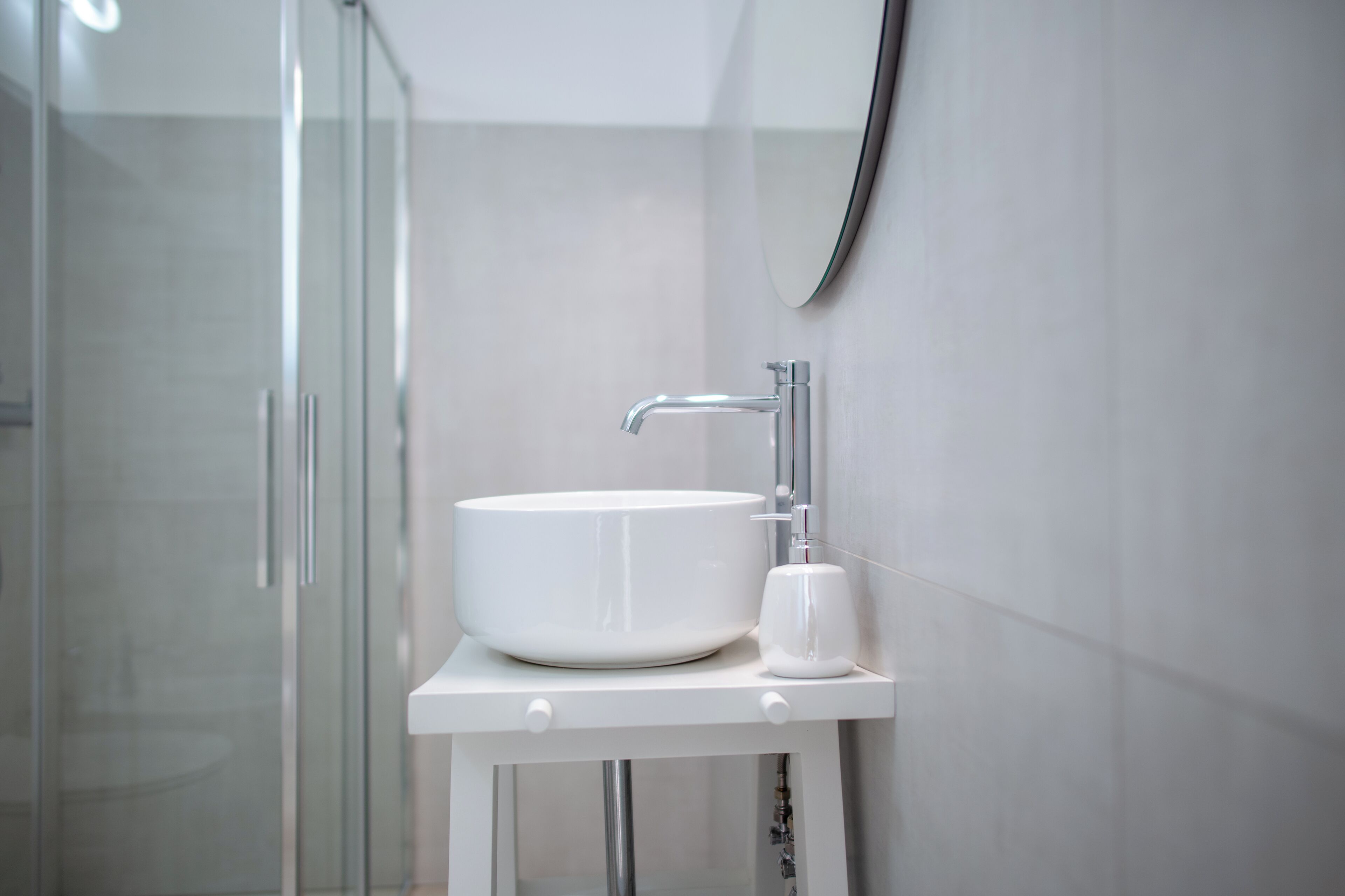 Un bany modern amb un lavabo blanc, un mirall i una cabina de dutxa de vidre.