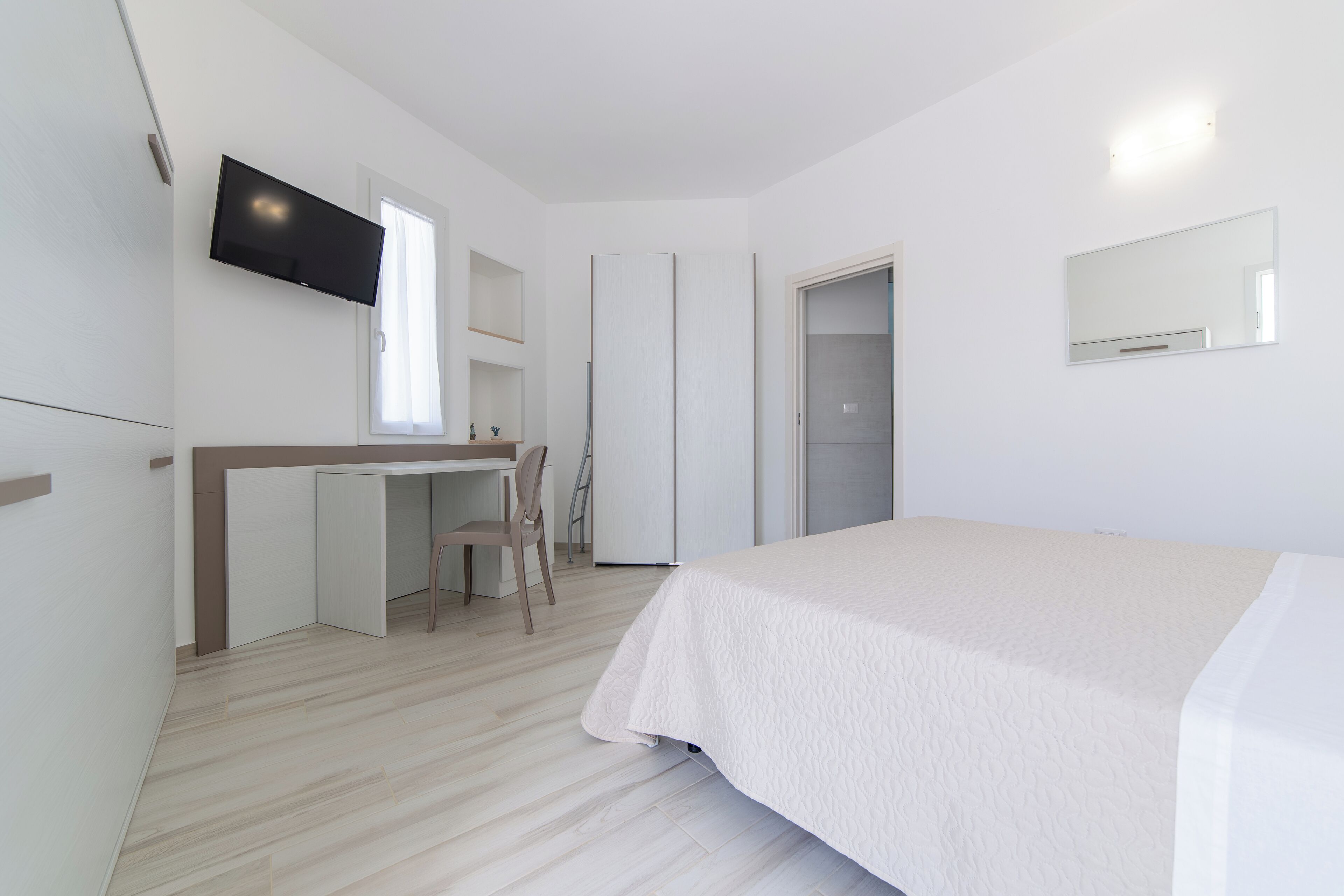 A bedroom with a bed, a desk, a chair, a TV, and a door.