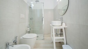 Un baño moderno con ducha de vidrio, un lavamanos blanco y un inodoro.