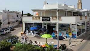 Un edificio de dos pisos con balcón, locales comerciales y mesas al aire libre.