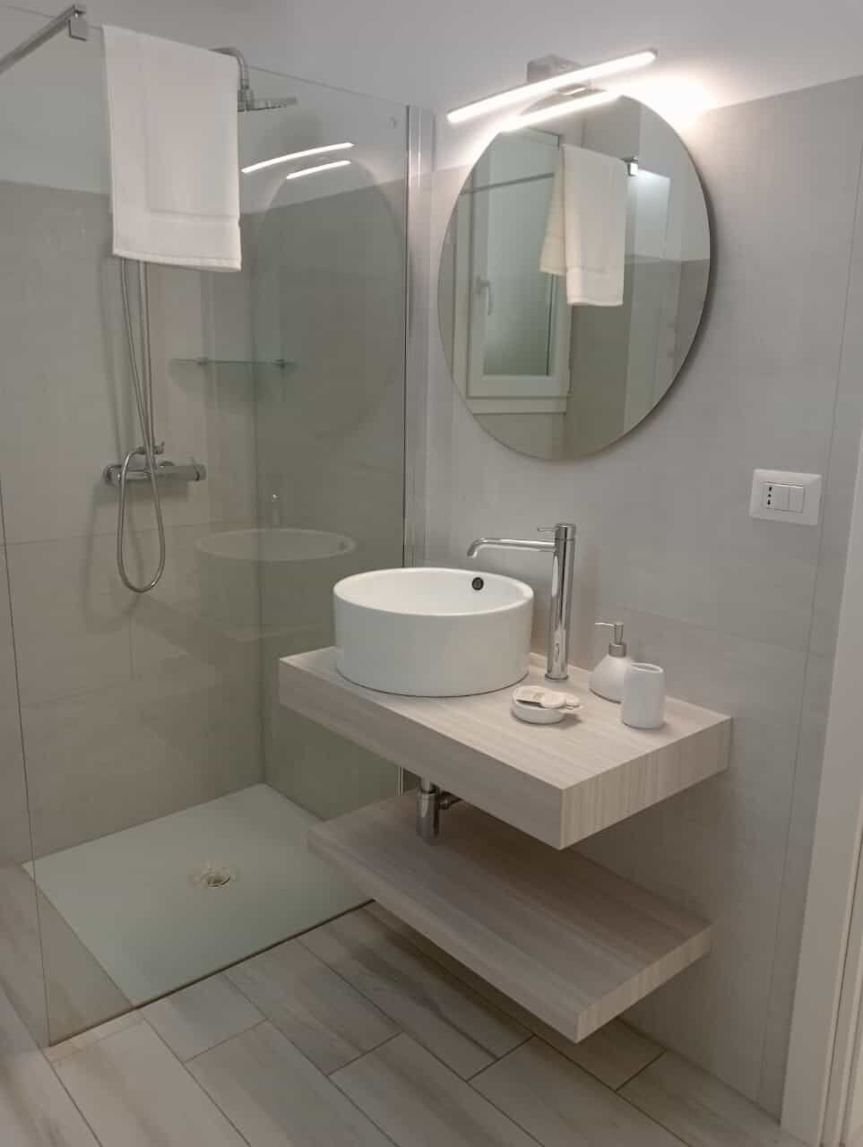 Un baño moderno con ducha de vidrio, espejo redondo y lavamanos blanco.