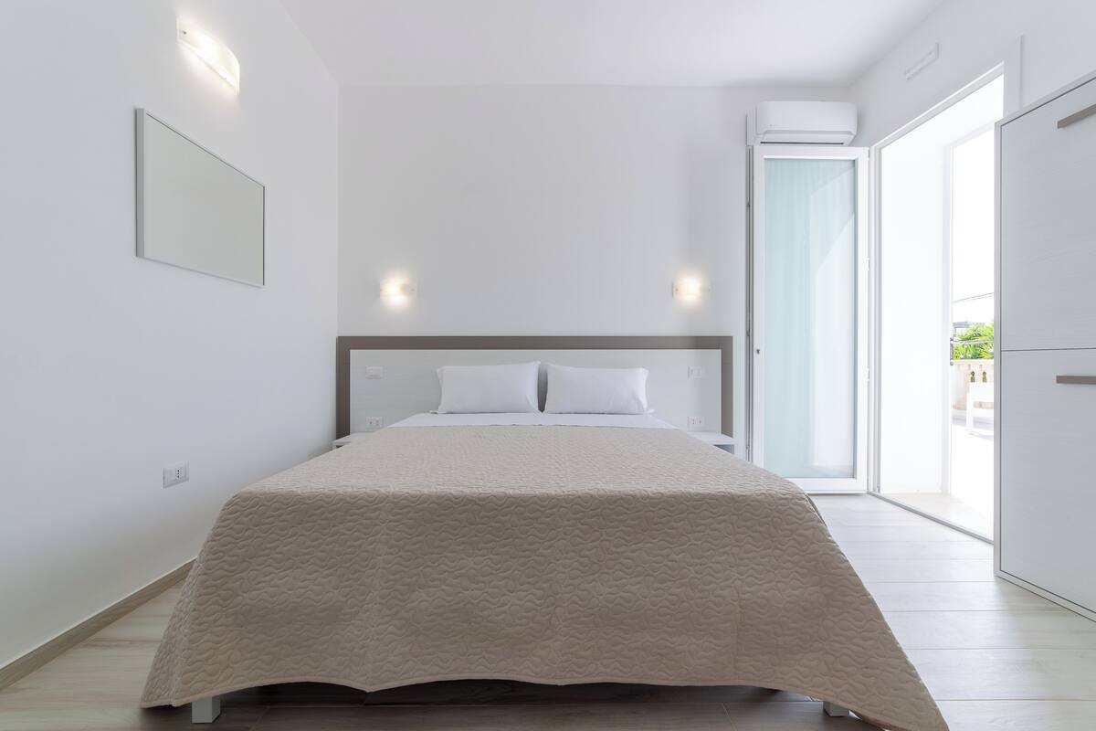 Un dormitorio moderno con una cama grande, un cabecero y un ventanal corredero que da a un balcón.