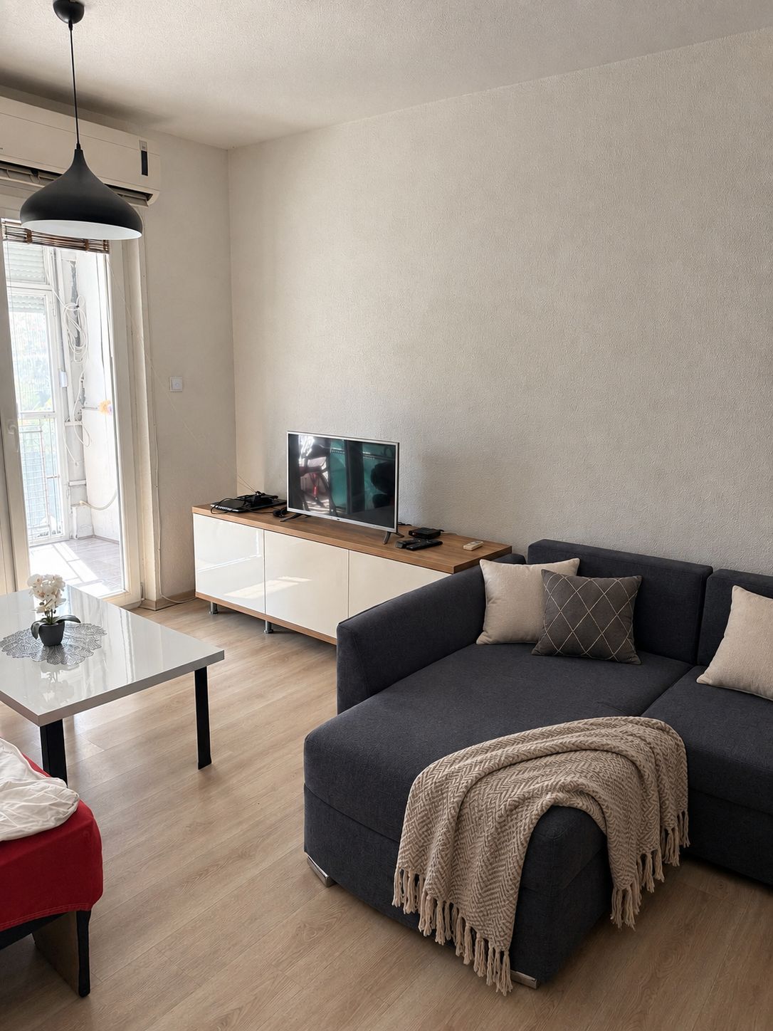 A modern living room with a dark sofa, a glass coffee table, and a television on a wooden cabinet.