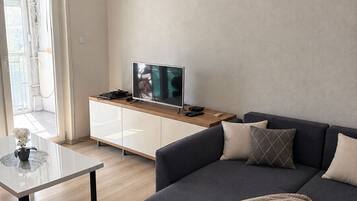 A modern living room with a dark sofa, a glass coffee table, and a television on a wooden cabinet.