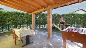 Une terrasse extérieure avec une table dressée pour le repas, une cheminée en briques et une table de baby-foot.