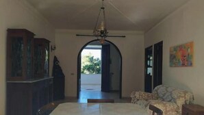 A dining area with a table and chairs, a chandelier, a cabinet, and a painting on the wall. - The house in the woods (Gorgofreddo)