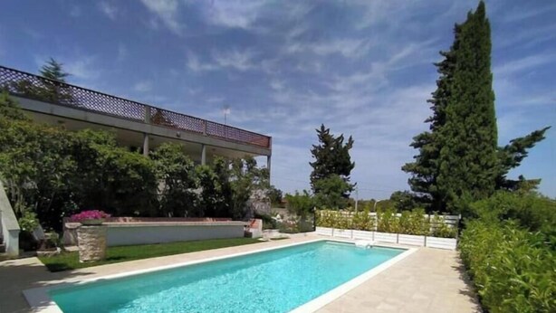 A rectangular pool with a tiled deck, surrounded by greenery and a building with a balcony. - The house in the woods (Gorgofreddo)