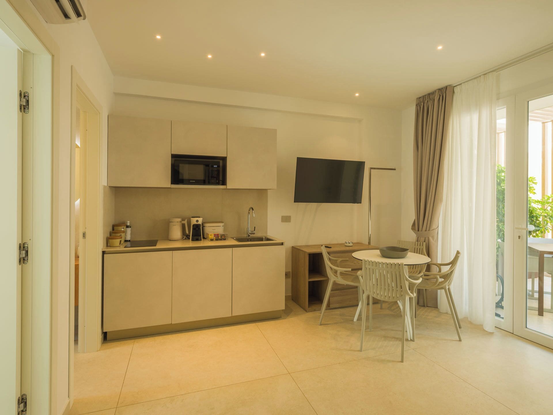 A compact kitchen with a microwave, coffee maker, and a flat-screen TV mounted on the wall.