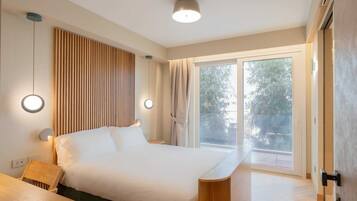Un dormitorio moderno con una cama grande, mesitas de noche, un escritorio y un ventanal corredero a un balcón.