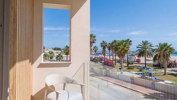 Ein Balkon mit weißem Stuhl, Blick auf Palmen und Strand, und ein klarer Himmel.