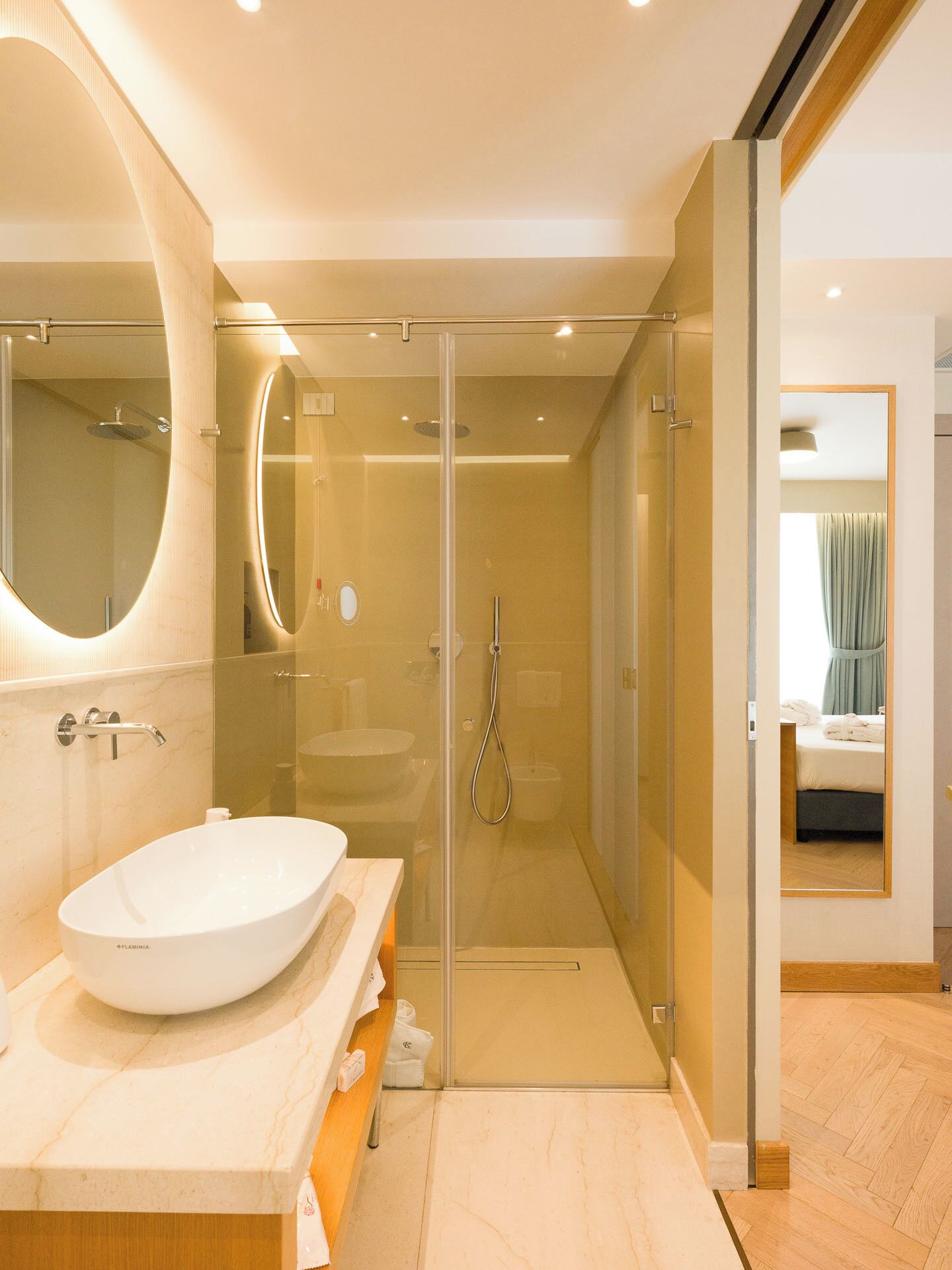 A modern bathroom with a large oval sink, a glass-enclosed shower, and a mirror with a wooden frame.