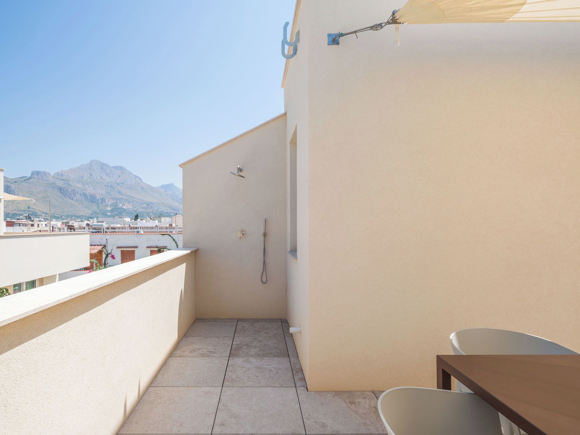 A small balcony with a shower, a table, and a chair.
