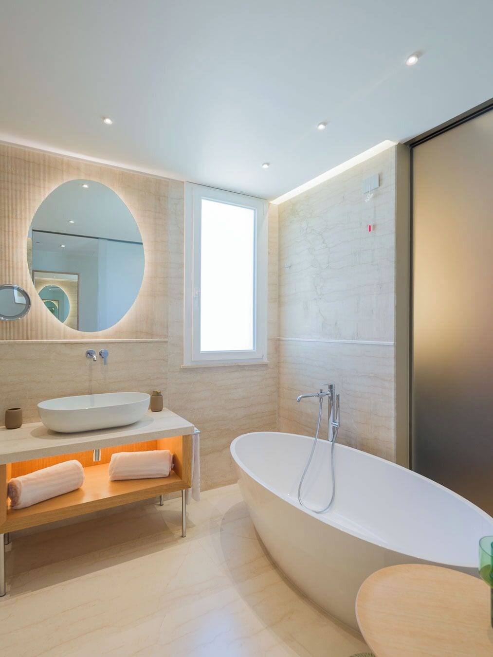 Un baño moderno con una bañera independiente, un espejo redondo y un amplio ventanal.